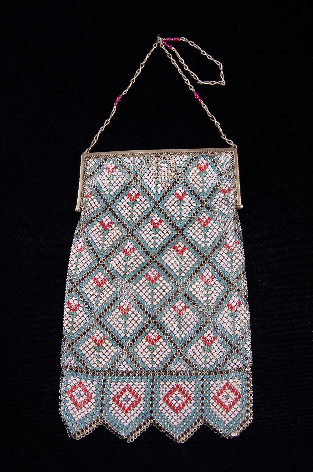 An Art Deco enamelled mesh evening bag with a silver frame, hanging from its chain against a black ground